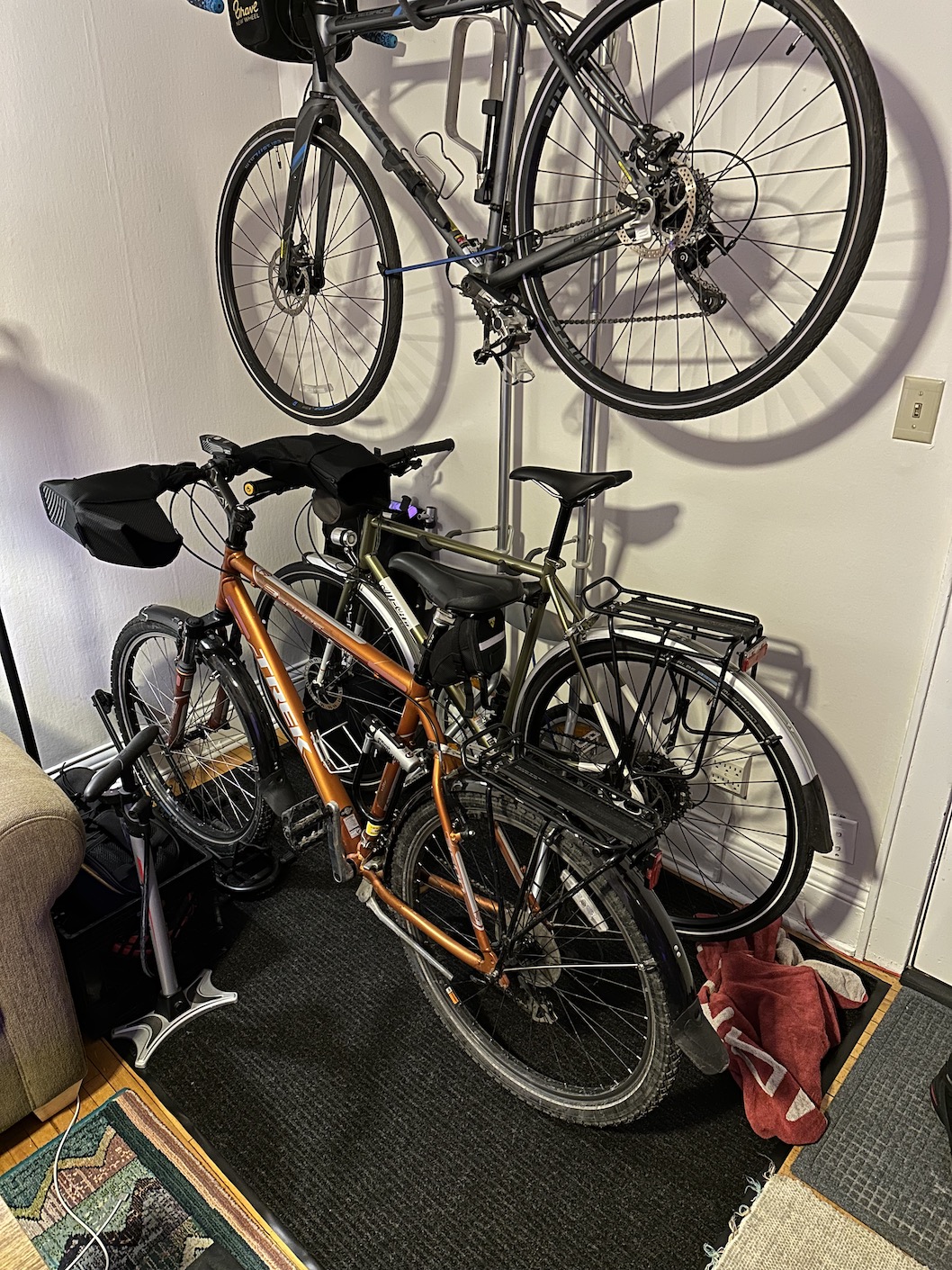 Two bikes are on a bike stand, one on top of the other, and a third is next to the stand, all on a 6 foot by 4 foot rug